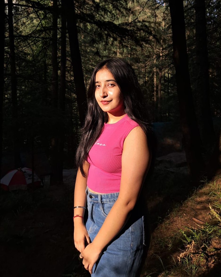 Saniya Sood in a pink top, standing in a sunlit forest